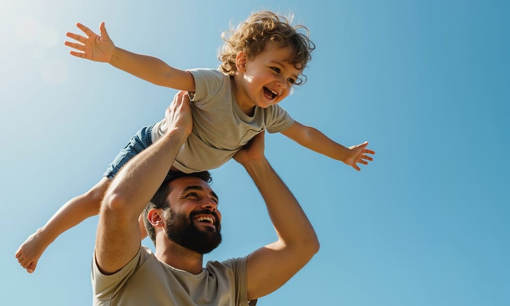Lafayette Guide to Universal Life Insurance Benefits - Happy Bearded Father Lifting Curly Haired Toddler Son With Arms Spread Against Blue Sky